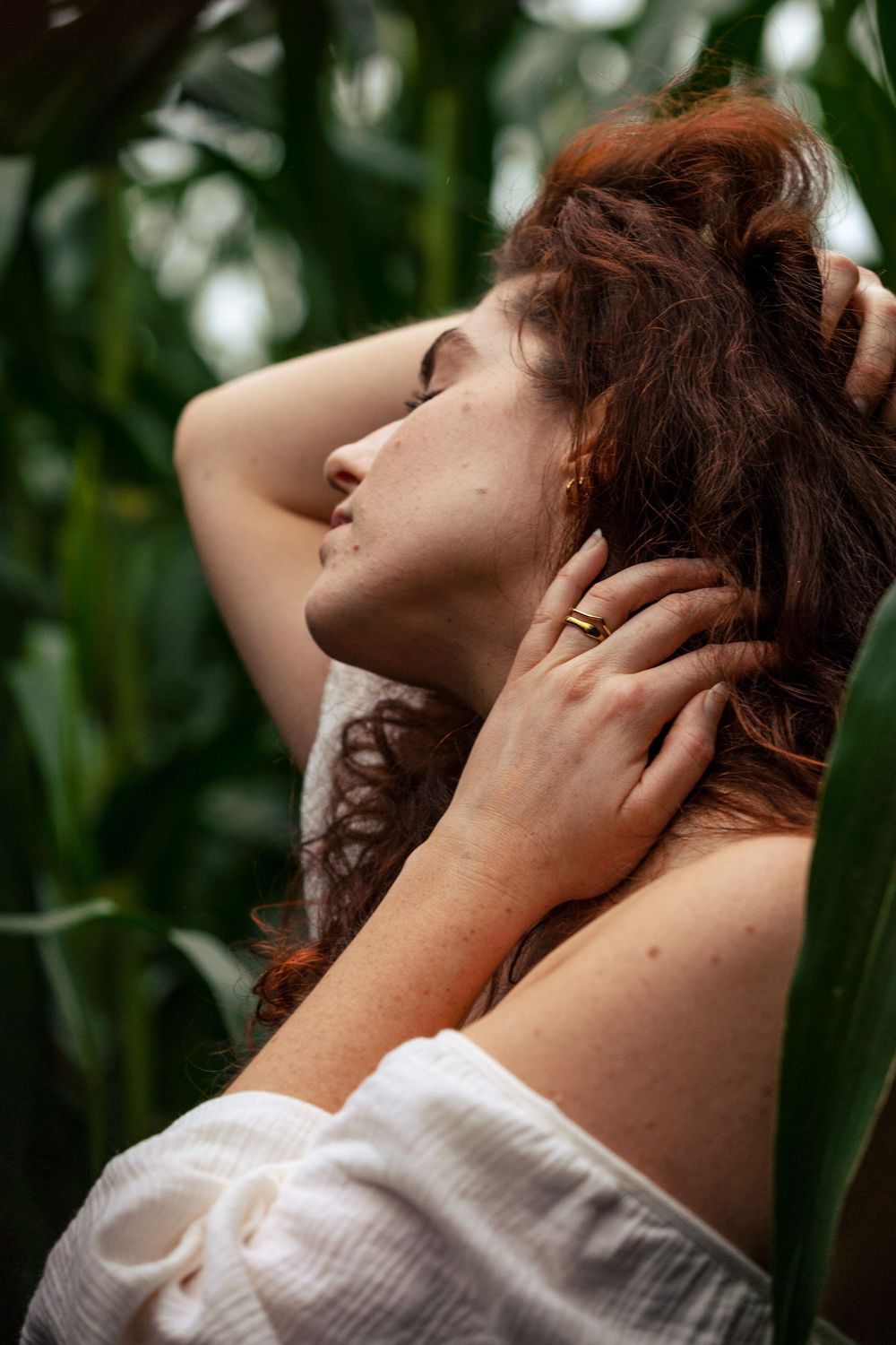 Een foto close uo van een vrouw. Ze heeft een hand in de nek en een hand in het haar. Ze heeft een jurk aan met blote schouder