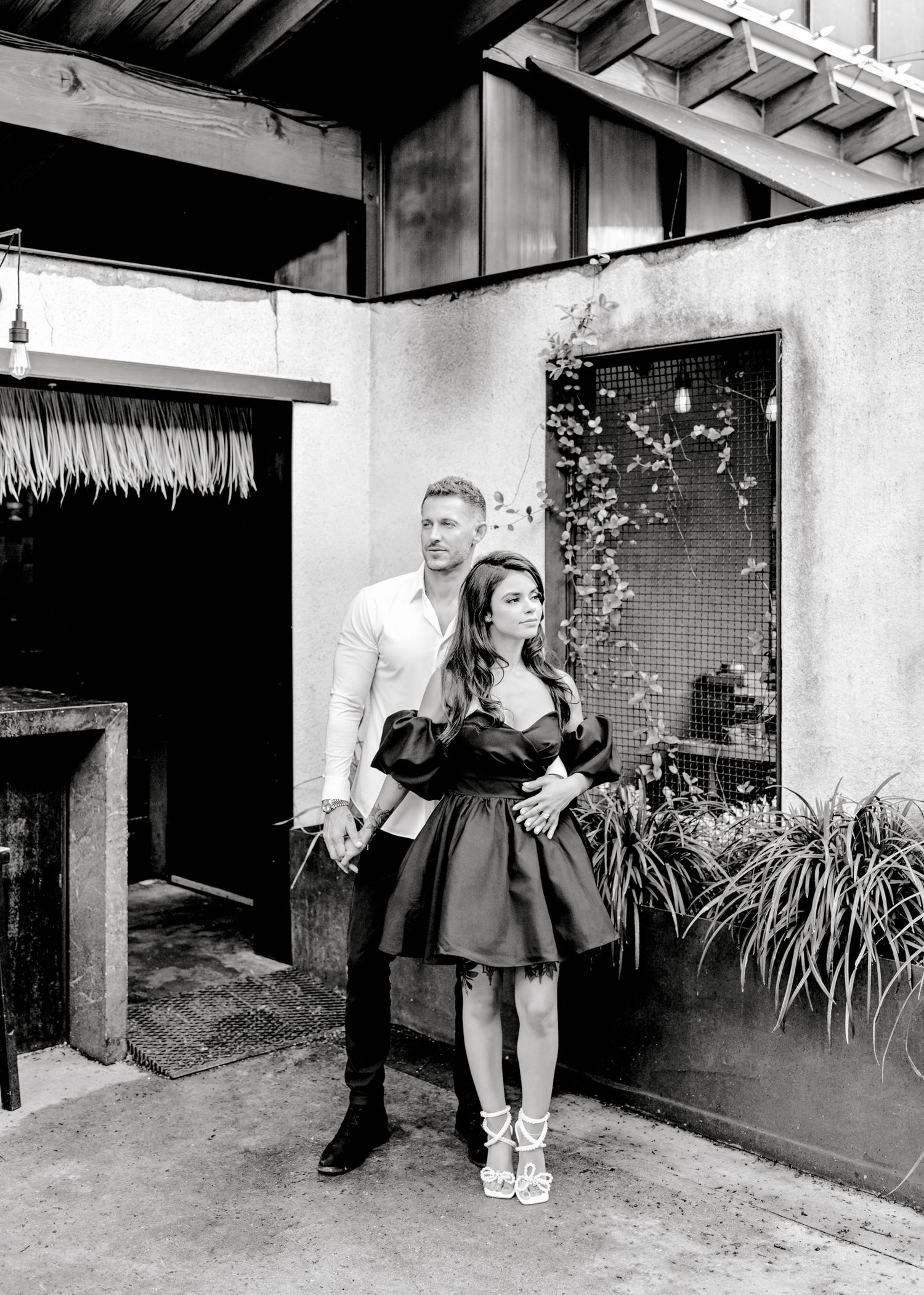 A sequence of five black and white photographs showing people playfully posing against a building wall with plants.