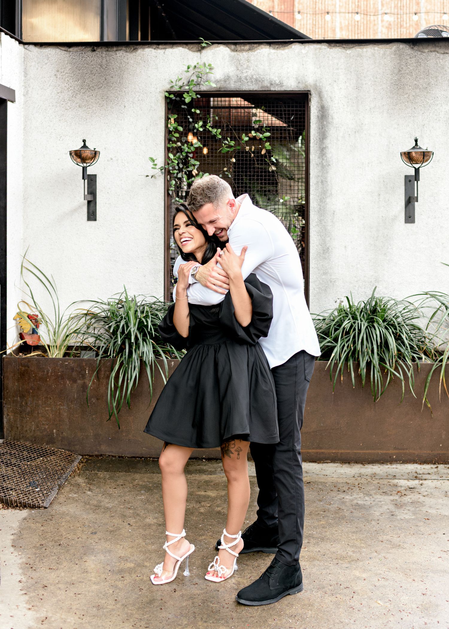 Romantic moment captured against white wall with climbing vines and decorative lanterns.