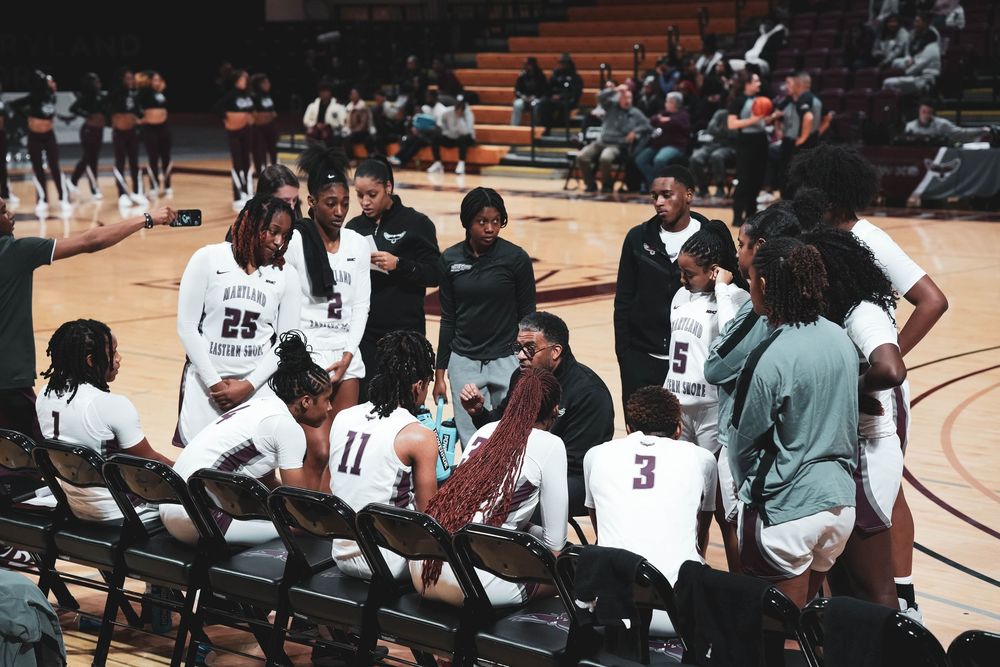 Basketball players and staff sit together on a bench during a game in a sports arena.