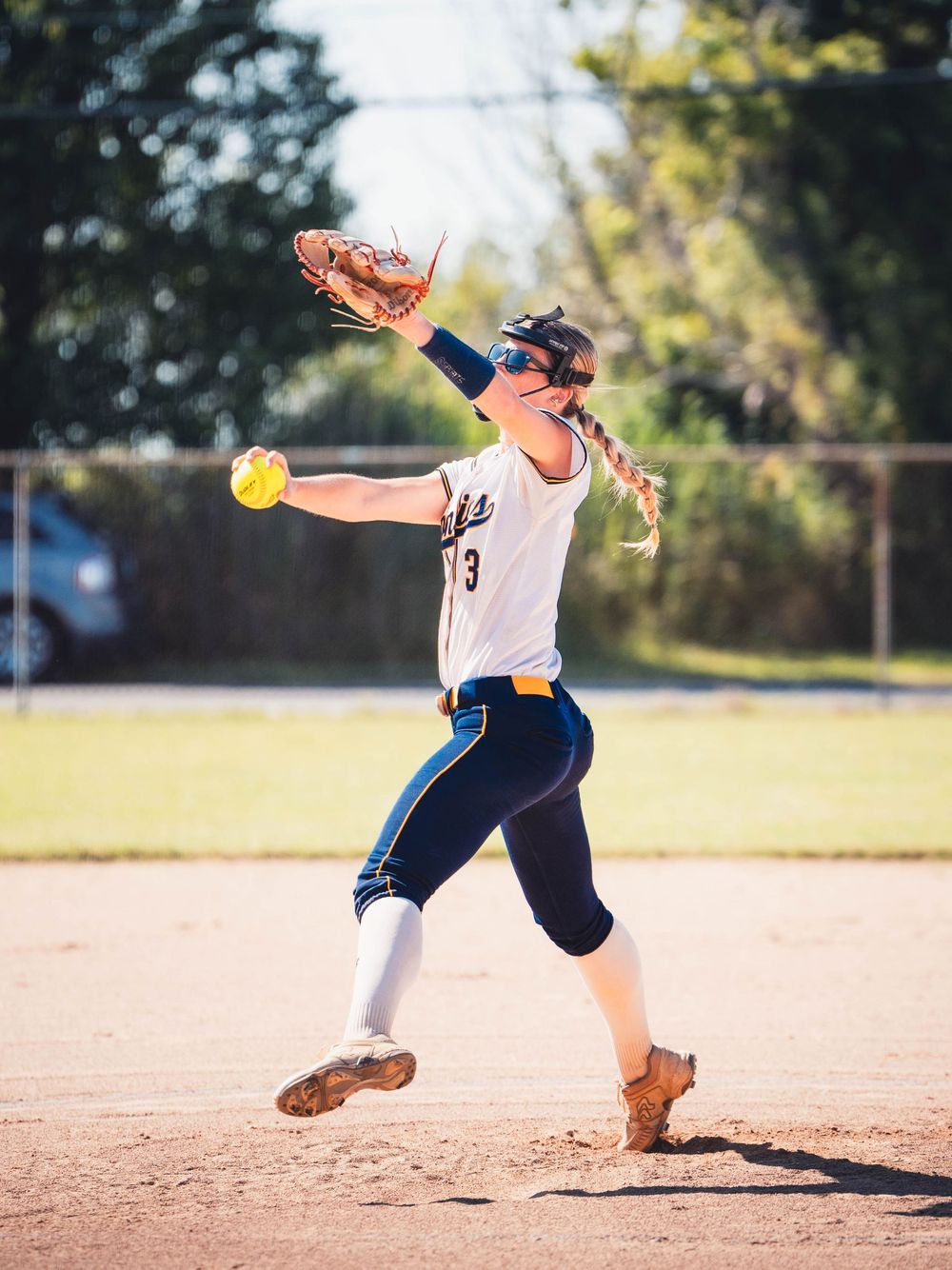 Softball player in mid-pitch delivery shows perfect form with dynamic movement on a sunny field.