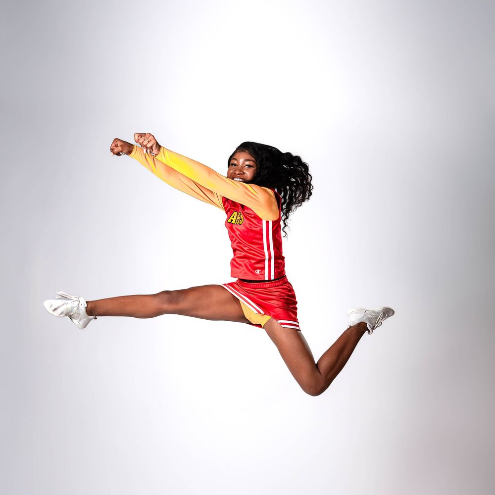 A dynamic figure in red and gold performs a stunning aerial jump with arms and legs extended in a dance pose.