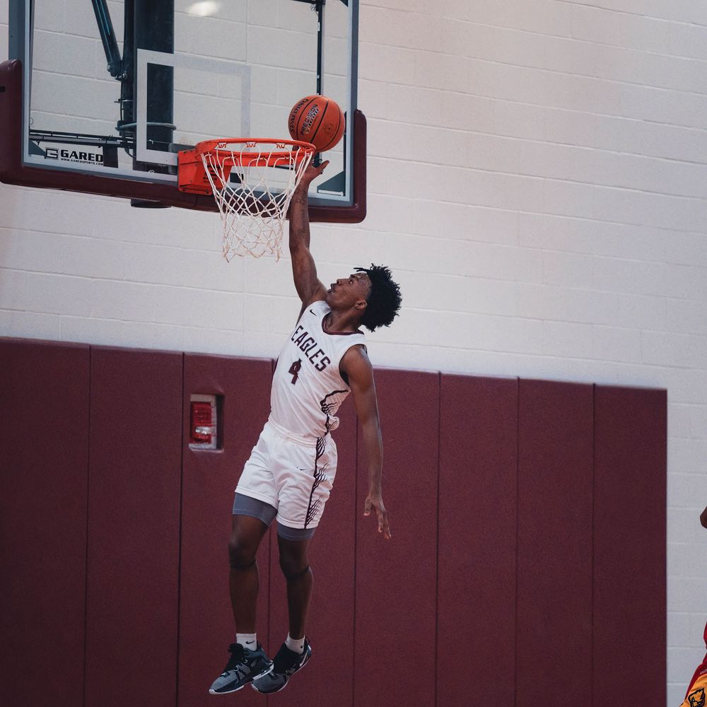 Basketball player in white jersey soars through the air for a powerful dunk attempt during a game.