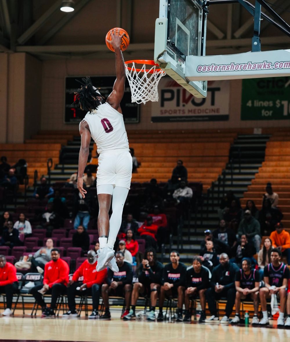 Basketball player in white jersey number 0 soars high for a dunk during a game in an indoor arena.