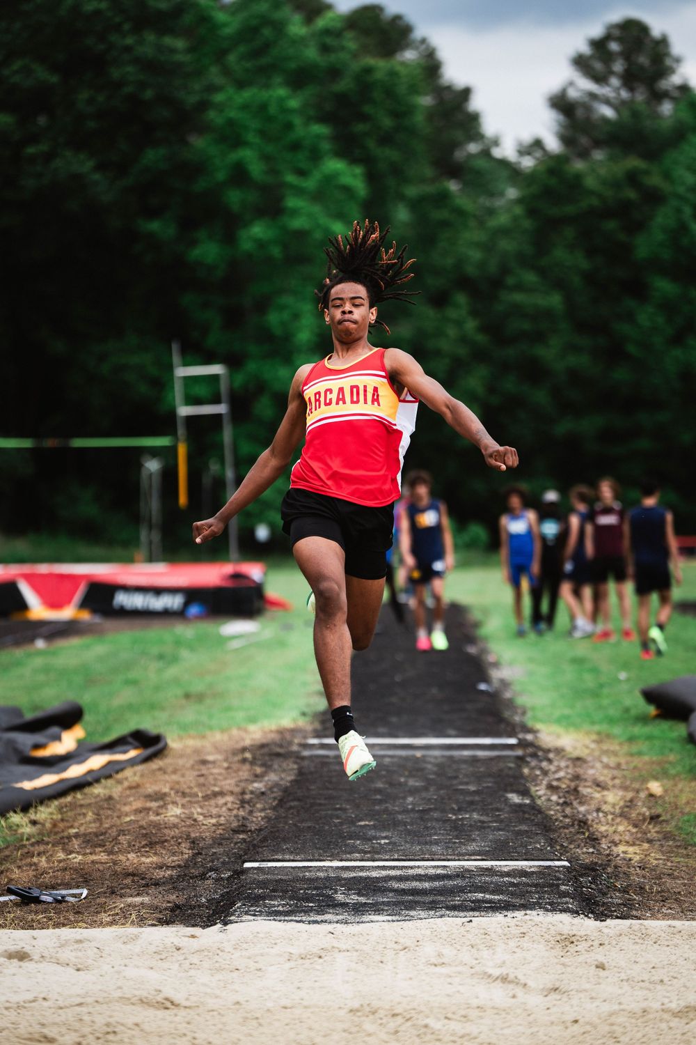 Track and field athlete performs triple jump sequence on long jump runway during outdoor practice.