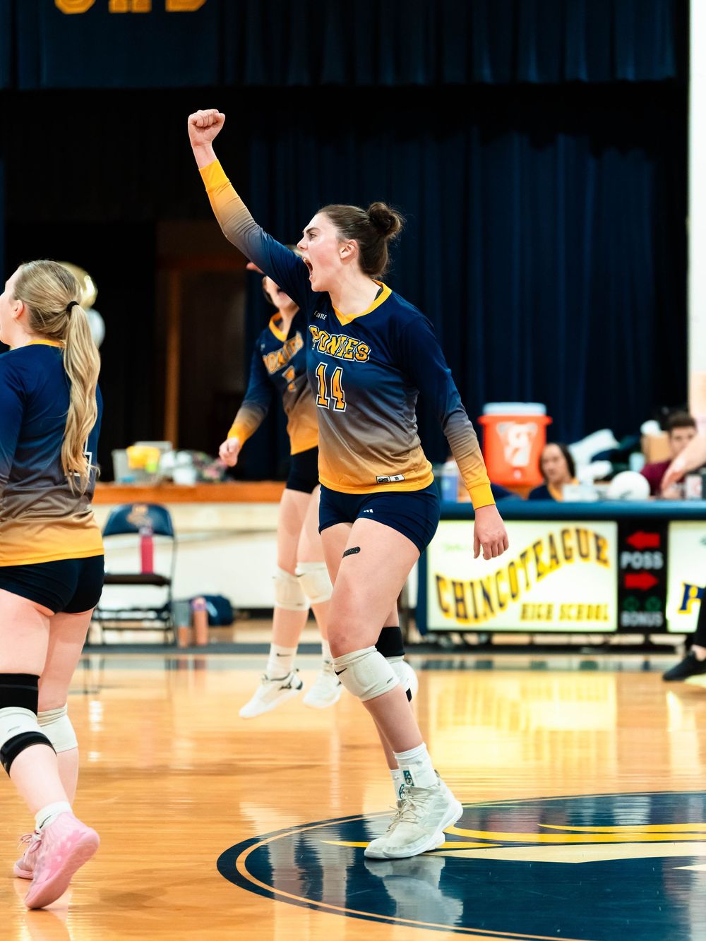 Multiple volleyball players leap and dive during an intense match on an indoor court.