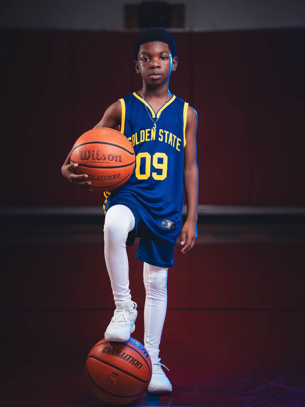Young basketball player in Golden State Warriors jersey poses with basketball for sports portraits.