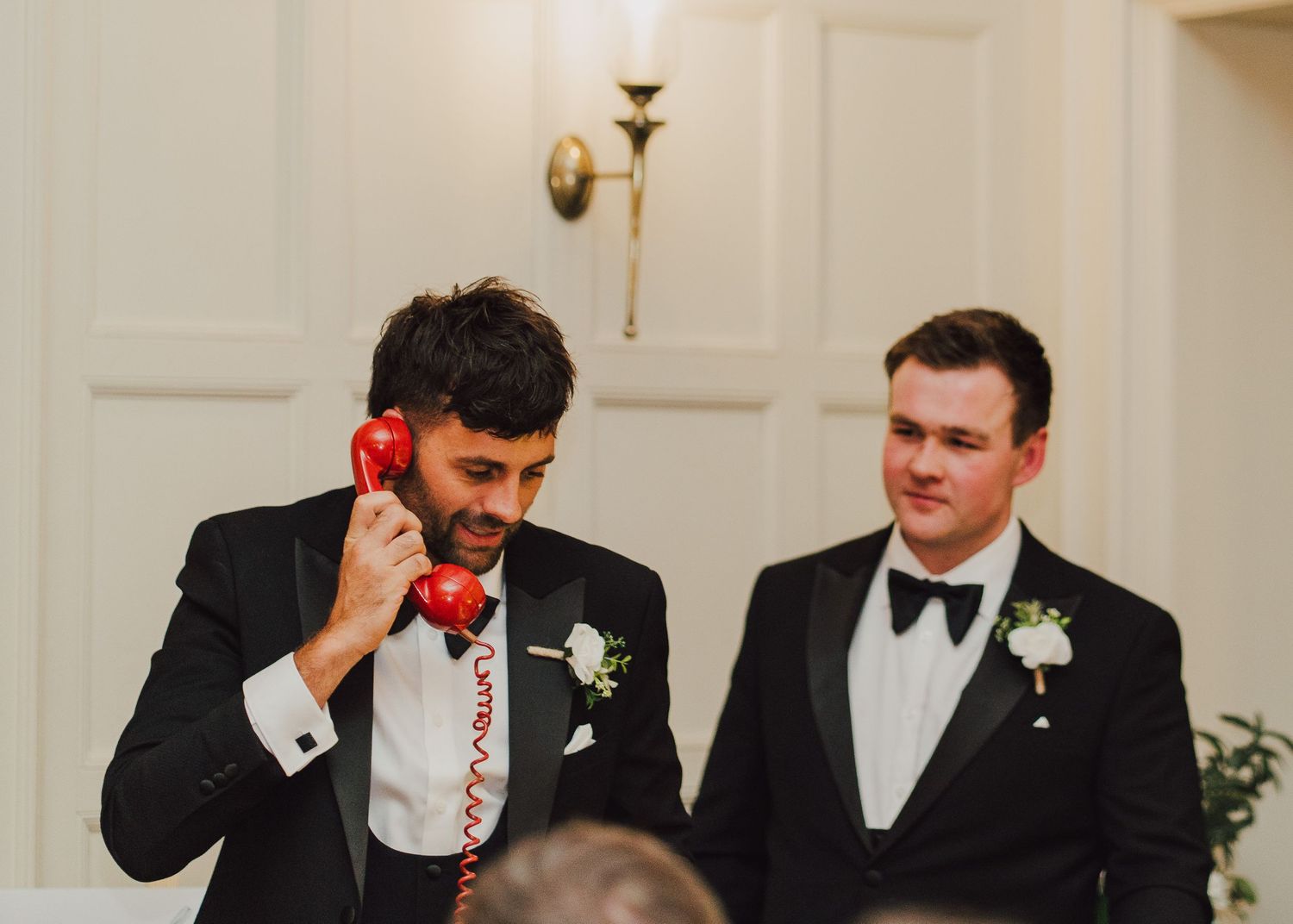 At a formal event, groomsmen wearing black tuxedos laugh and smile together in a candid moment.