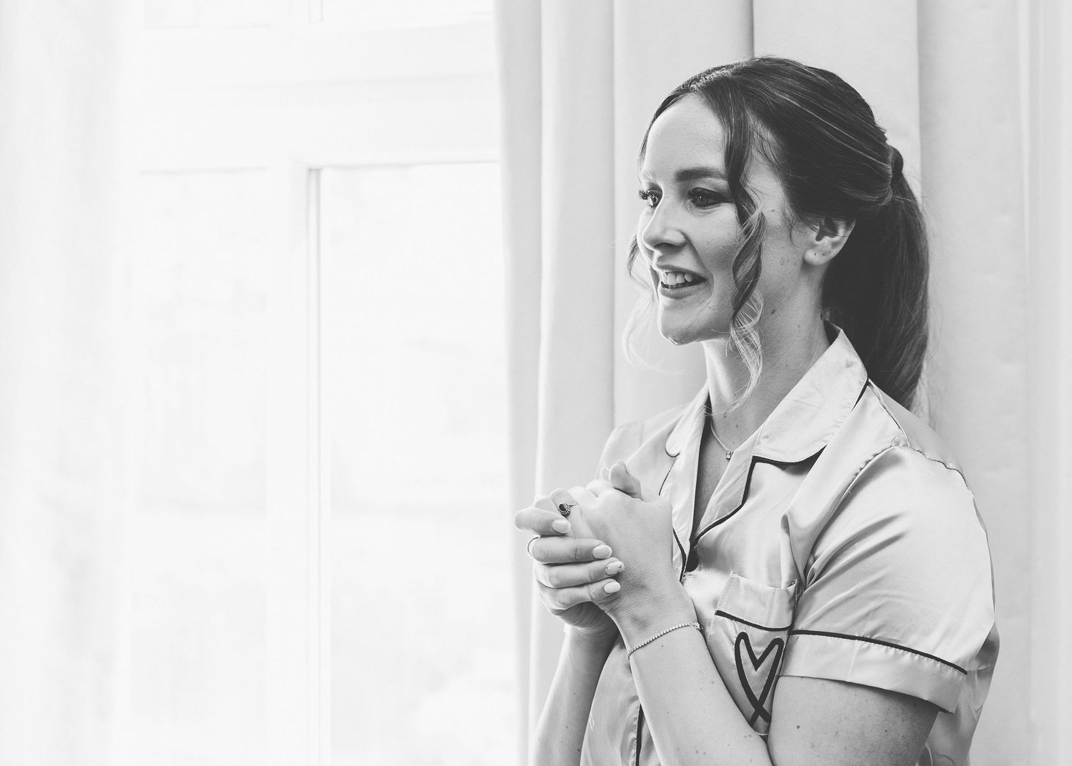 Black and white image of someone in a button-down uniform laughing and gesturing while standing against a light wall.