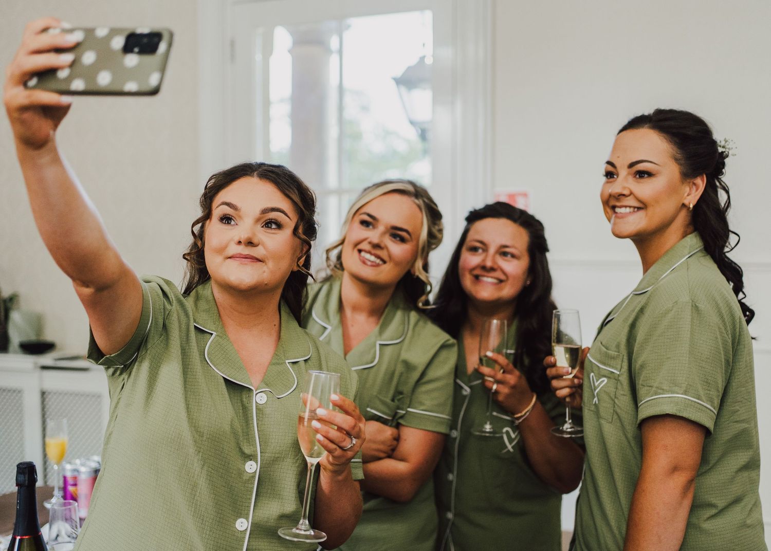 Healthcare workers in green scrubs holding champagne glasses take a celebratory selfie together.