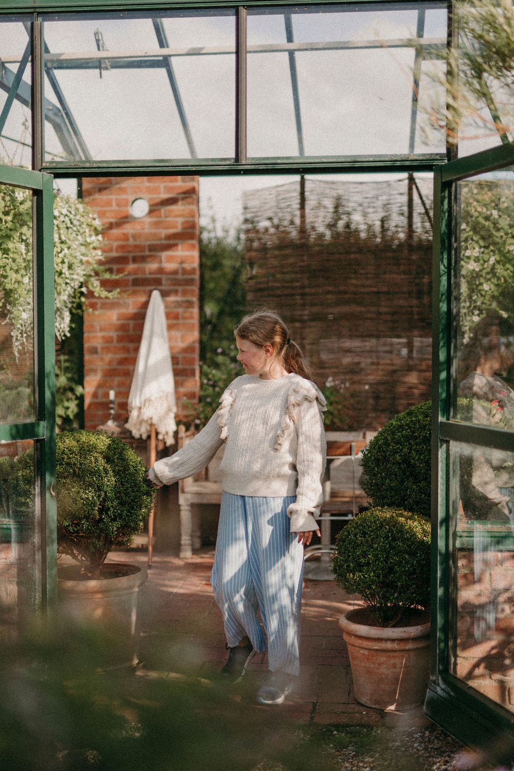 Four connected greenhouse images showing a bright morning sunlight filtering through glass panels and potted plants.