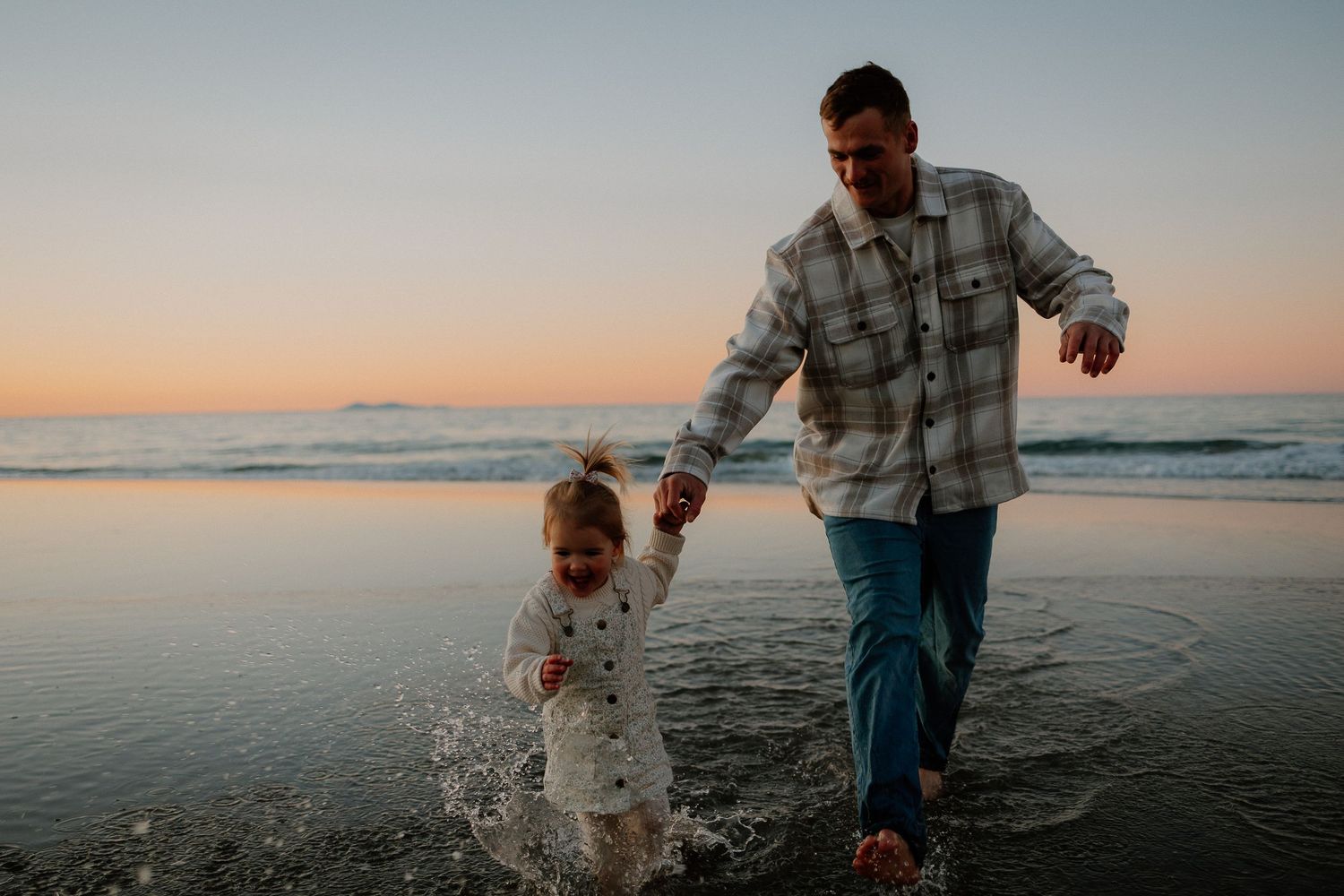 Family enjoying a sunset beach walk along the shoreline while splashing in the shallow ocean water at dusk.