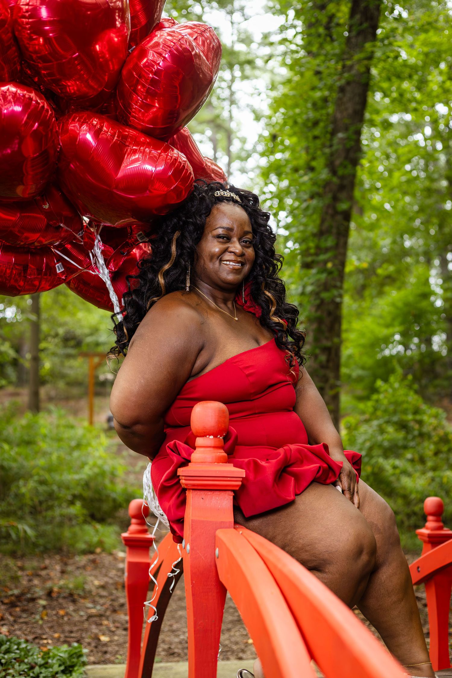 Festive outdoor portrait session with red heart balloons and an orange bench in a wooded setting.