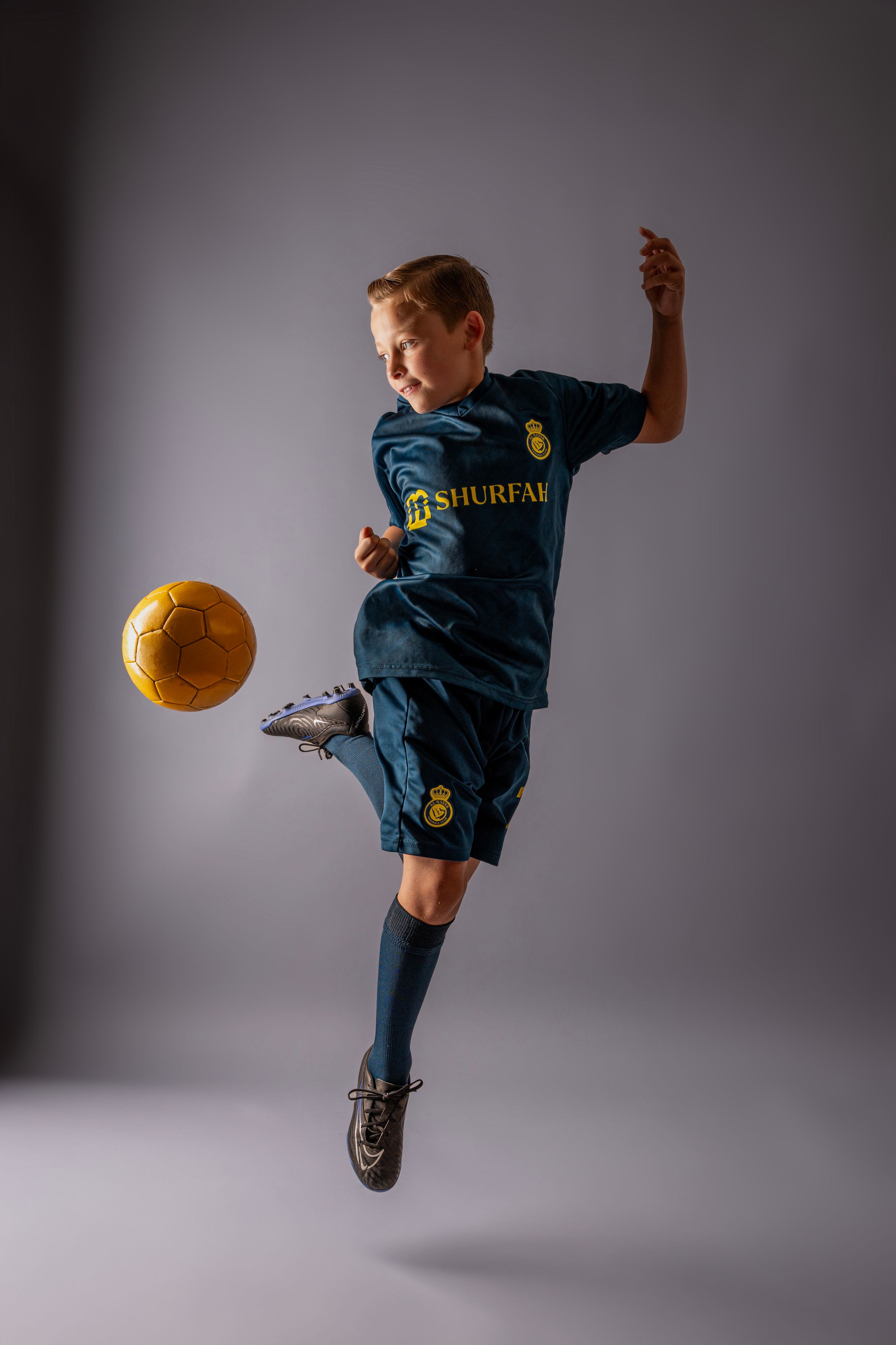 Young soccer player in blue jersey performs acrobatic kick with yellow ball in dynamic action sequence.