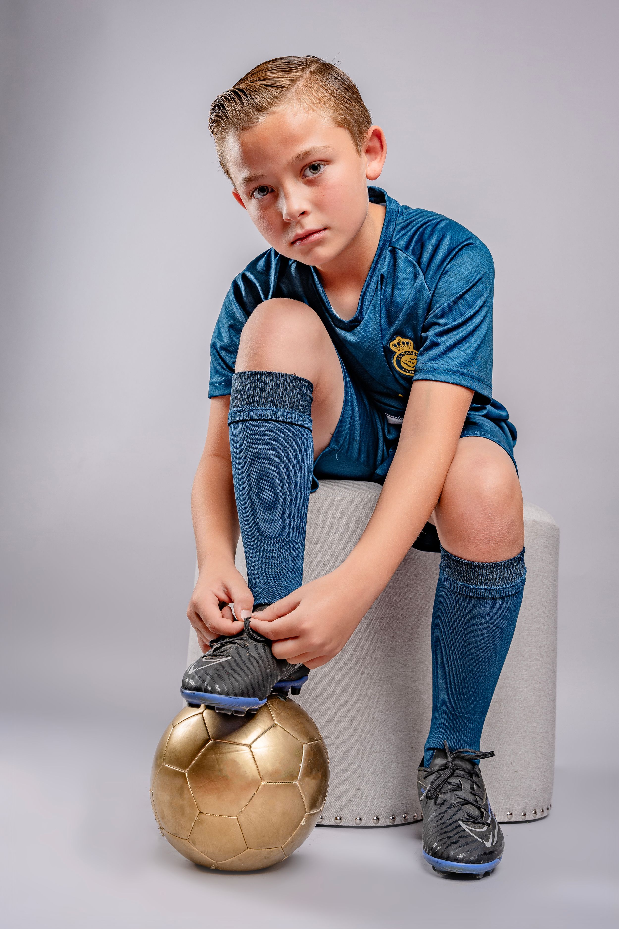 Artistic sequence showing a person in blue uniform crouching with a gold soccer ball on gray background.