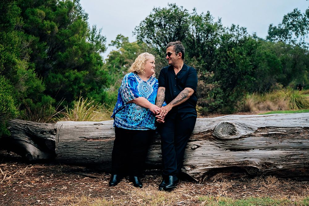Couple shares intimate moment while seated on rustic wooden log in natural outdoor setting.