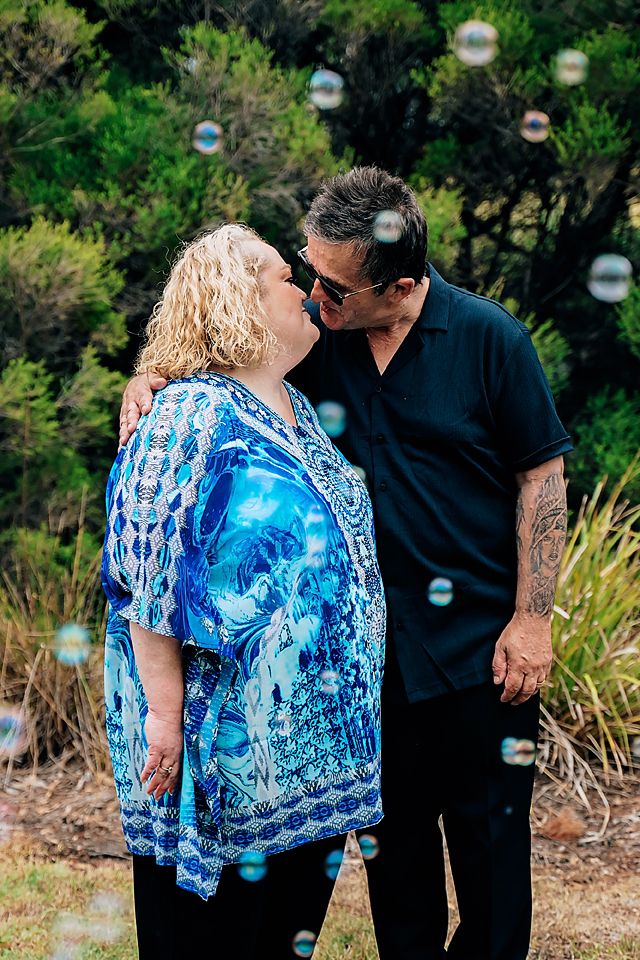Romantic outdoor photoshoot featuring a couple in blue kaftan and black shirt with floating bubbles in the background.