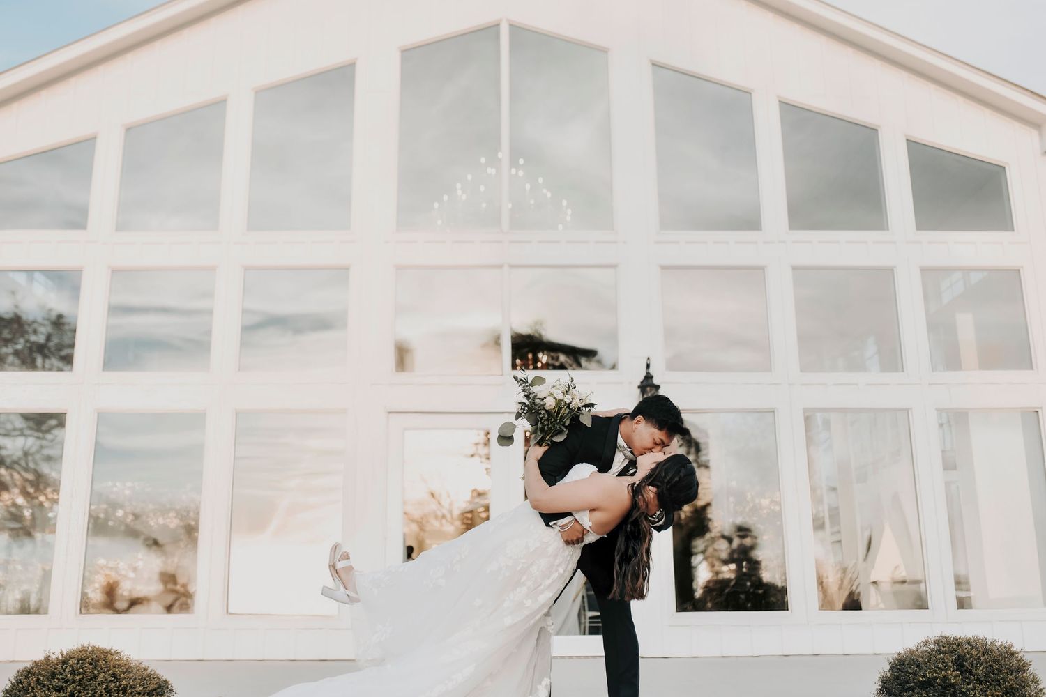 a groom dips his bride in front of the glass windows at firefly gardens wedding venue