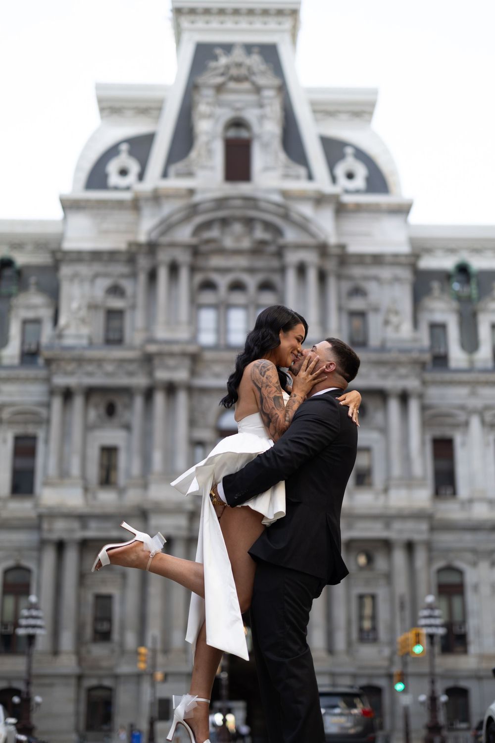 A couple embraces in front of Philadelphia City Hall in a series of romantic wedding photos with ornate architecture behind them.