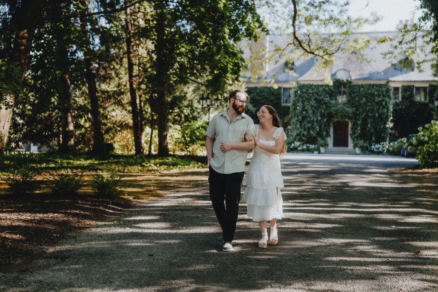A couple walking along a tree-lined path on a sunny afternoon.