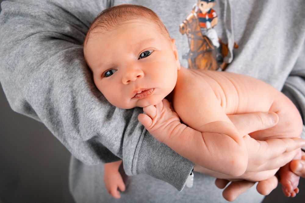 Series of gentle black and white portraits showing a newborn baby wrapped in soft gray fabric.