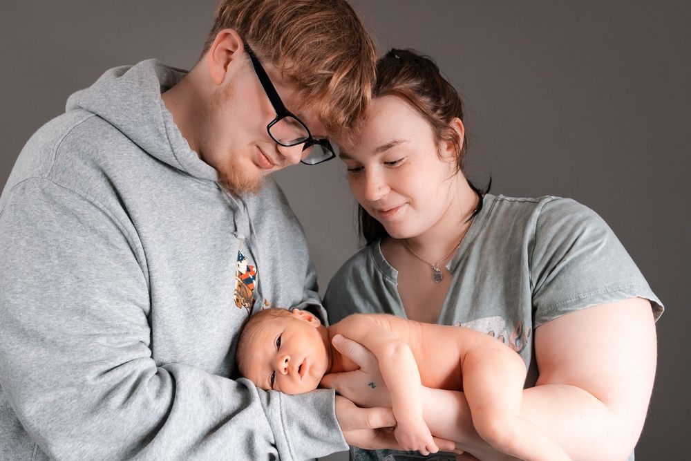 Loving family moment showing tender interaction with newborn baby wearing gray and neutral color clothing.