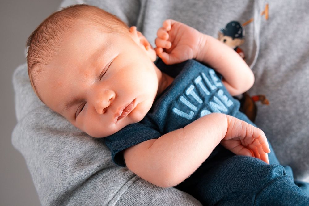 Sleeping newborn baby swaddled in gray and blue blankets during a professional photo session.
