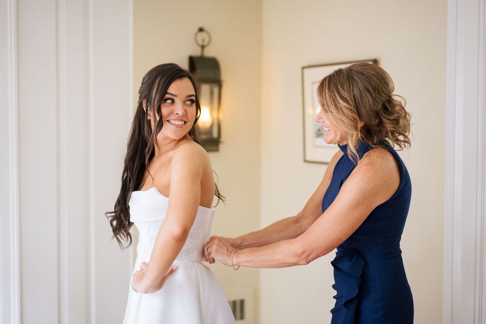 Women in formal attire preparing in a bright, sunlit room before a special event.