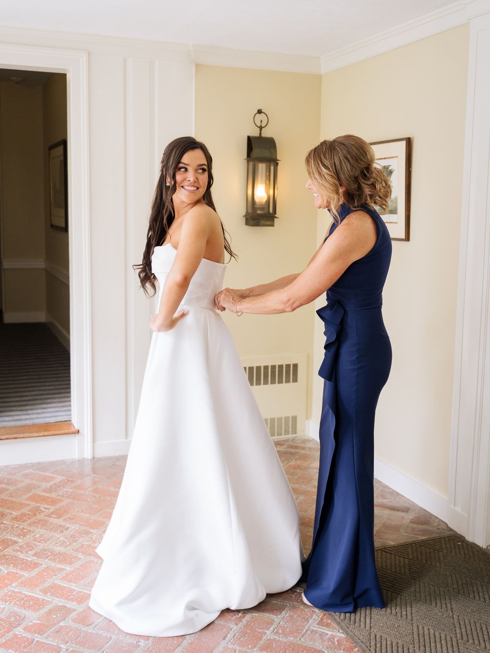 Wedding preparations show a stunning white bridal gown being adjusted in an elegant indoor setting.