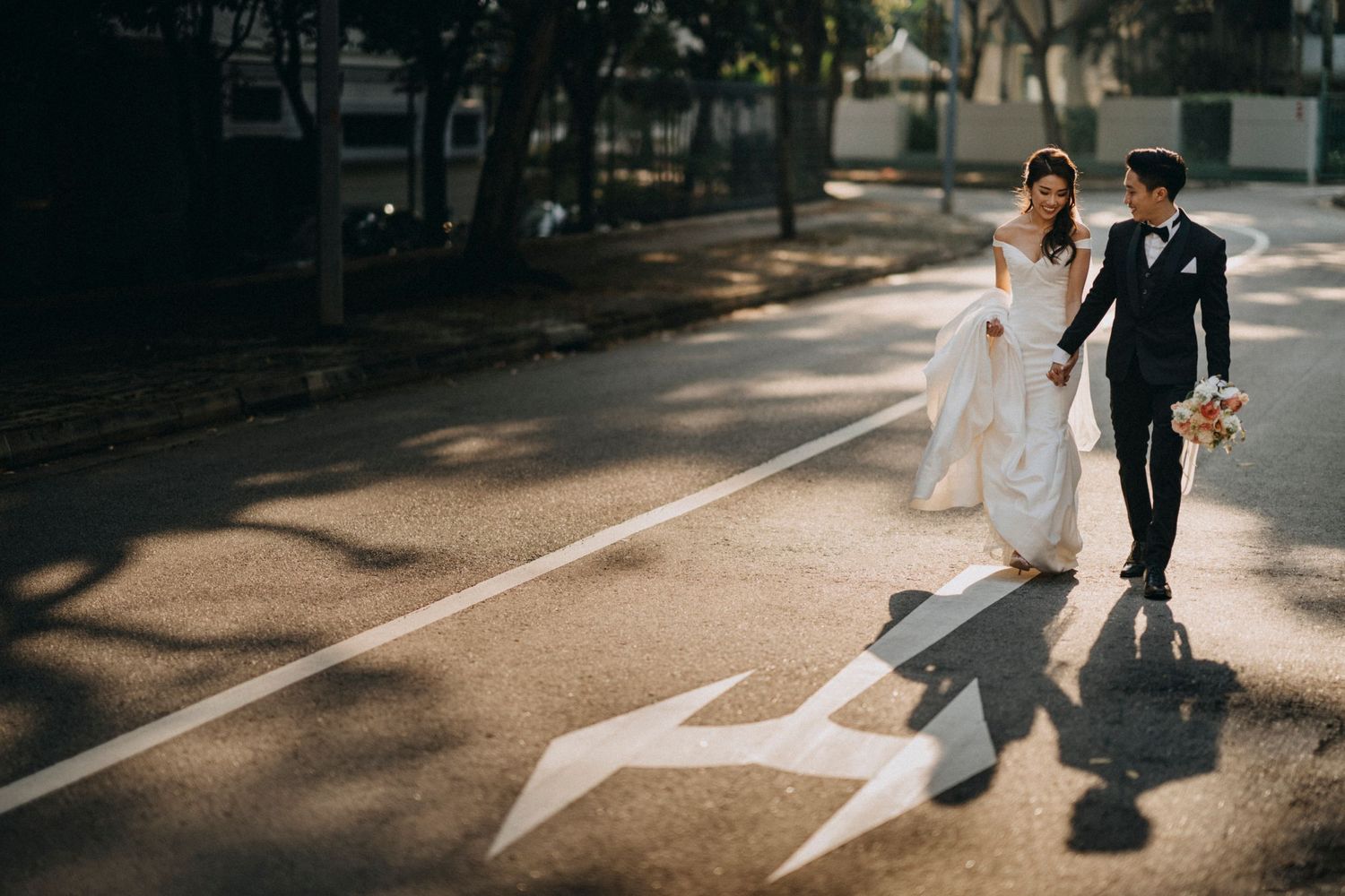 Couple walks hand in hand on street while their shadows stretch ahead of them.