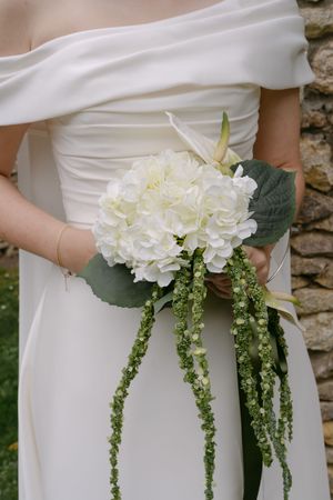 Row of white hydrangea bouquets with cascading greenery held against white dresses.