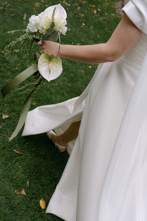 Elegant white wedding dress details with floral bouquet against a grassy backdrop.