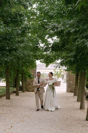 Wedding party walks along a tree-lined path in an outdoor garden setting.