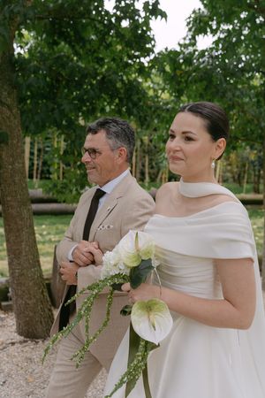 Bride in elegant white dress holds a bouquet of white calla lilies and greenery.