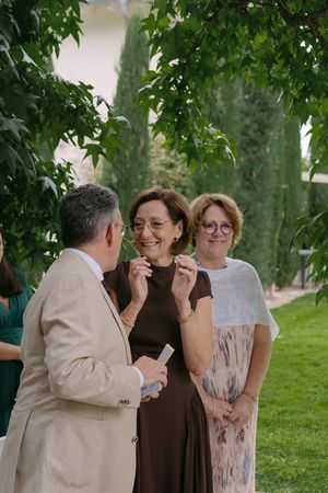 Wedding guests in brown and beige attire share laughs during outdoor celebration.