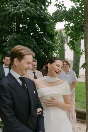 Wedding couple sharing genuine laughter during their outdoor ceremony with guests in background.