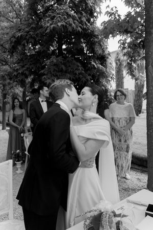 Black and white photo of a romantic wedding kiss in a garden setting.