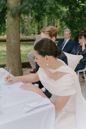 Bride signing wedding documents at an outdoor ceremony table.
