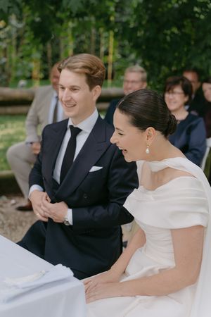 Wedding couple sharing a joyful moment during outdoor ceremony with guests in background.