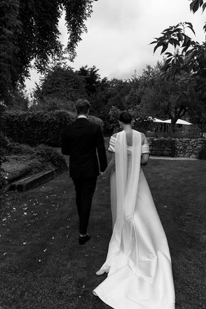 Black and white photo of couple walking through garden path with flowing wedding dress.
