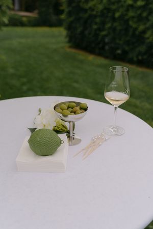 Elegant white table setting with wine glasses and green olives at an outdoor event.