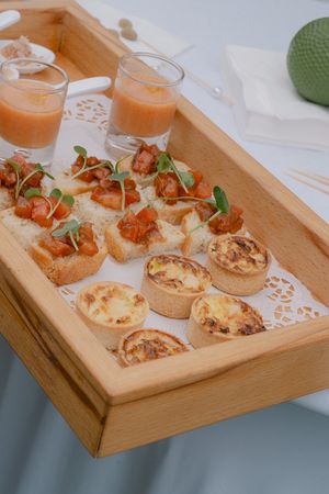 Wooden serving tray with appetizers and orange cocktails arranged for catering service.