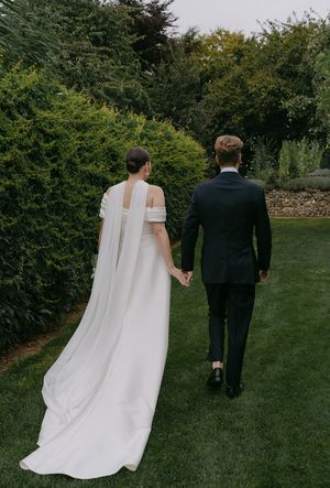 Couple walking on garden path with bride's dramatic white dress train flowing behind.