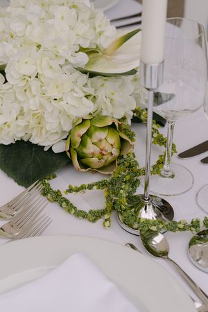 Elegant white hydrangea flowers and greenery decorate a formal table setting with crisp white linens.