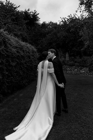 Black and white photo showcasing the dramatic train of a wedding dress during garden walk.
