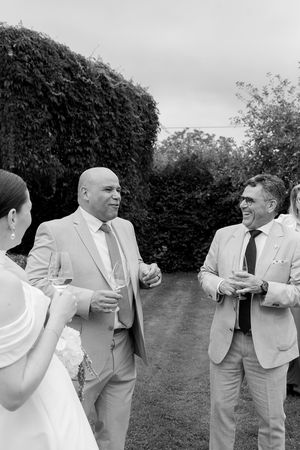 Wedding party members in light colored suits laugh and embrace during outdoor photo session.
