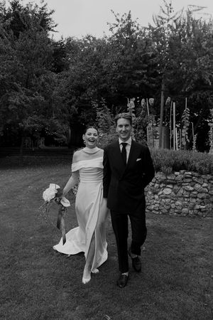 Wedding couple strolling through garden setting with stone wall backdrop.