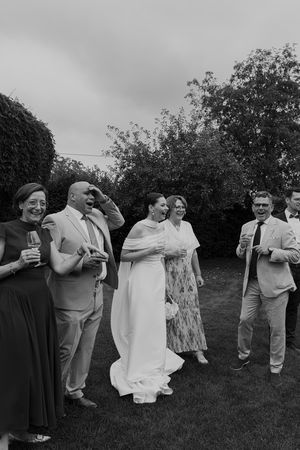 Wedding guests gather on a grassy lawn for group photos during an outdoor celebration.