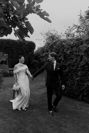 A black and white wedding photo showing a couple walking together on a garden lawn.