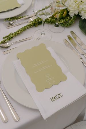Elegant place setting with gold menu card and white plate at wedding reception.